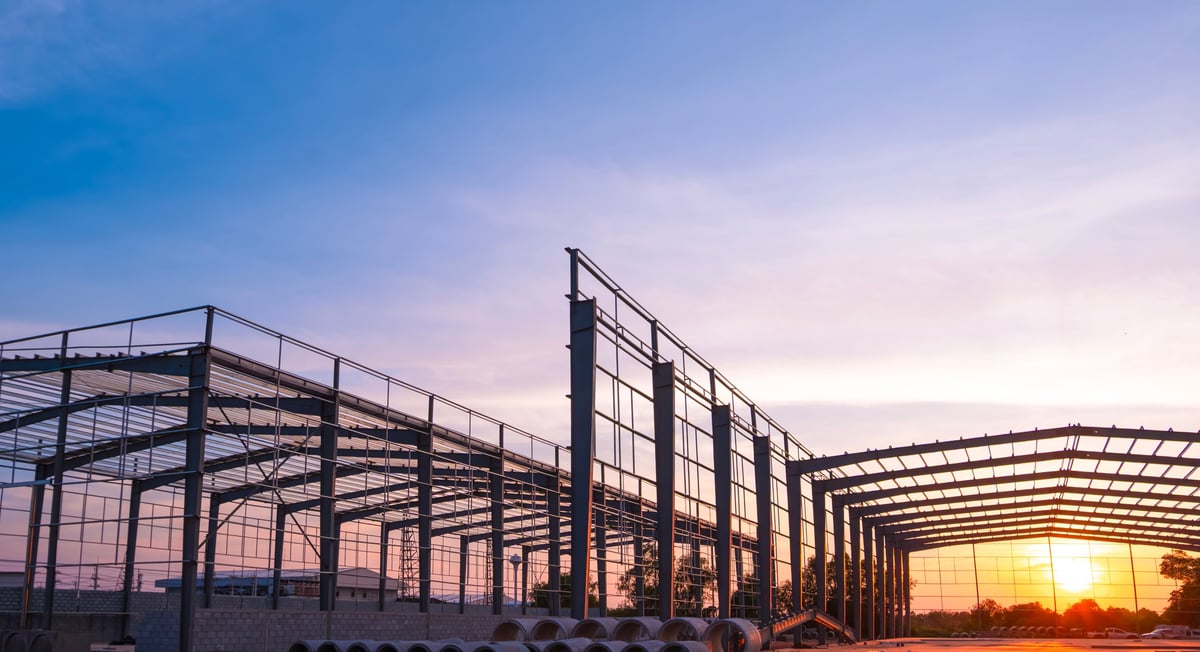 Silhouette steel structure of modern industrial factory building in construction site against sunset sky background, low angle view