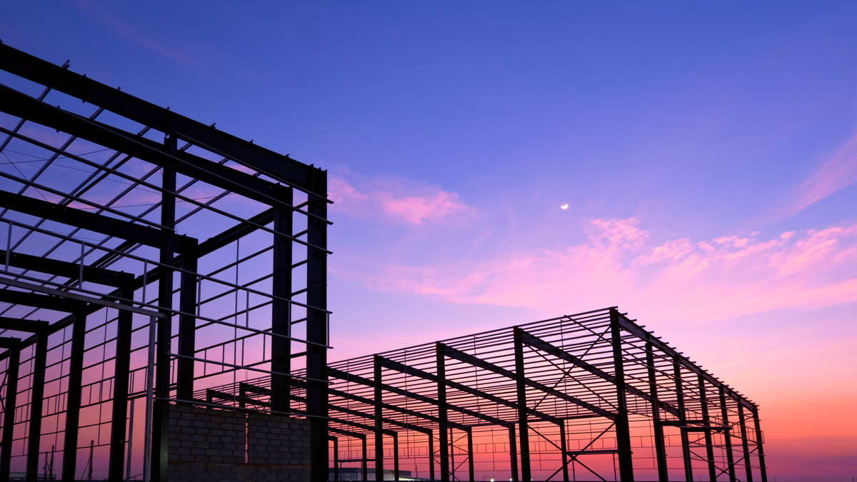 Silhouette metal structure of 2 industrial warehouse factory buildings framework in construction site against colorful twilight sky background