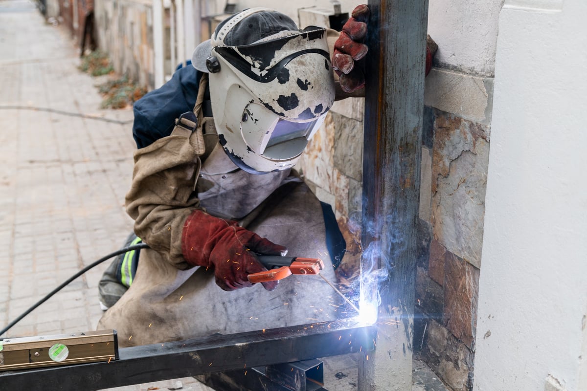 Welder wearing protective gear working on a metal column, creating sparks